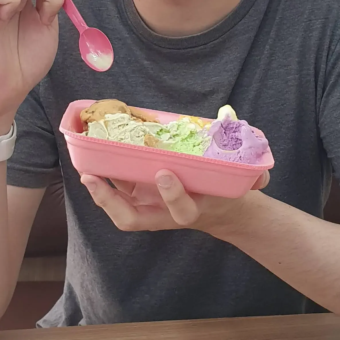 Pessoas segurando uma bandeja de isopor com 5 sabores de sorvetes coloridos e parcialmente consumidos